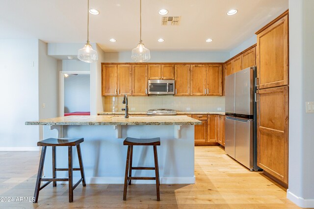 kitchen with appliances with stainless steel finishes, a center island with sink, light hardwood / wood-style floors, and pendant lighting