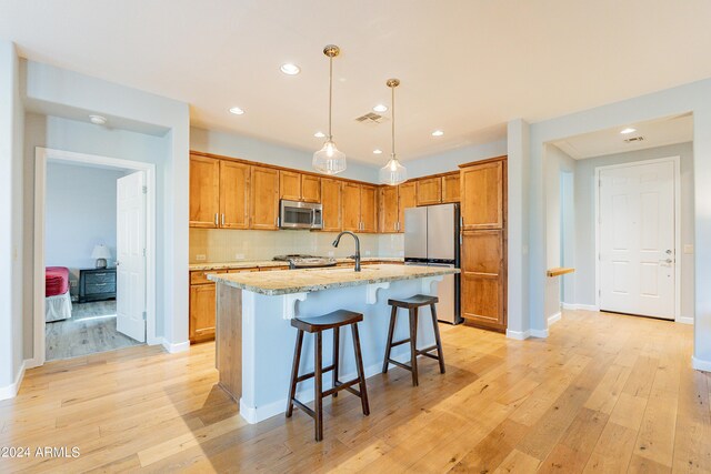 kitchen featuring pendant lighting, a kitchen island with sink, appliances with stainless steel finishes, a kitchen breakfast bar, and light wood-type flooring