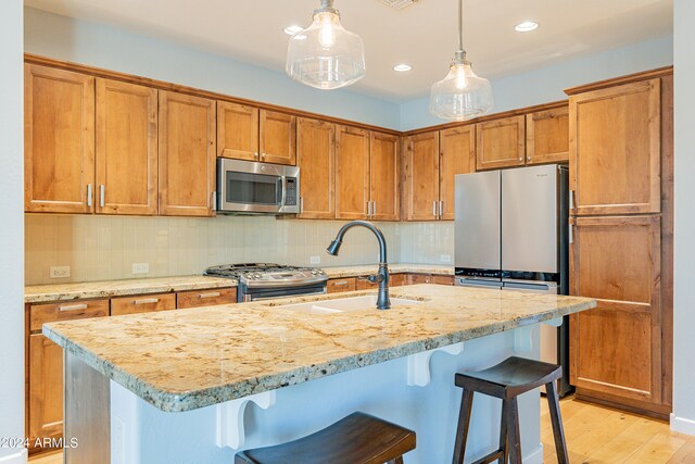 kitchen featuring appliances with stainless steel finishes, light wood-type flooring, a breakfast bar area, and an island with sink