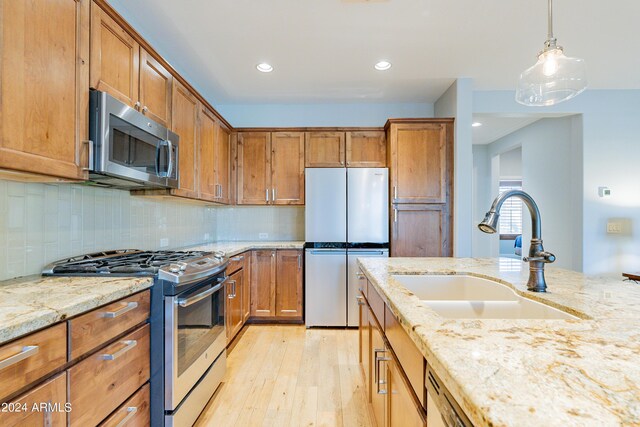 kitchen featuring pendant lighting, sink, stainless steel appliances, light hardwood / wood-style floors, and decorative backsplash