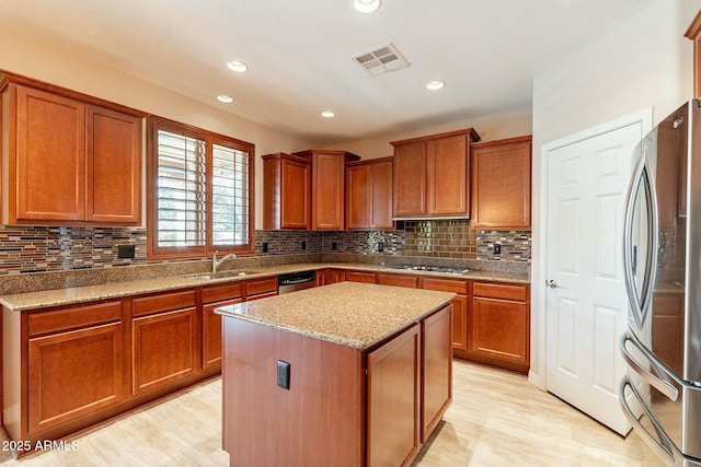 kitchen with visible vents, light stone counters, a center island, stainless steel appliances, and a sink