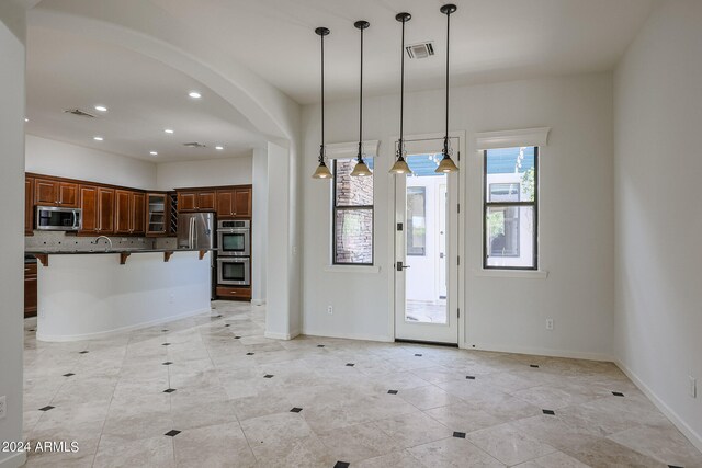 interior space with appliances with stainless steel finishes, backsplash, a kitchen island, pendant lighting, and a kitchen bar