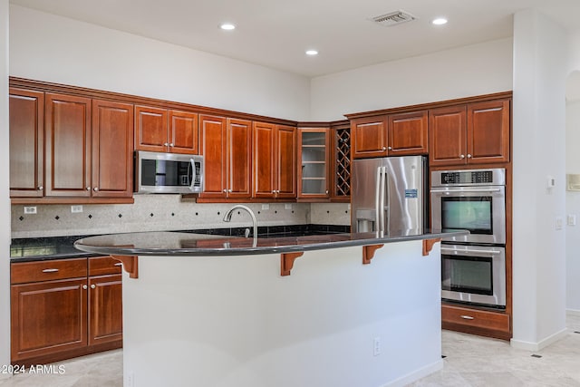 kitchen featuring a kitchen island with sink, appliances with stainless steel finishes, a kitchen bar, and decorative backsplash