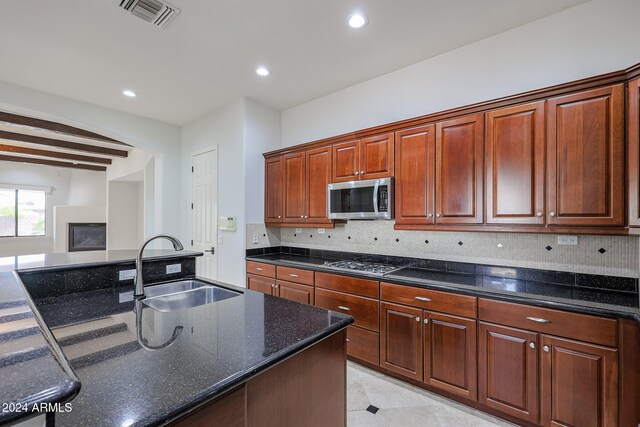 kitchen with appliances with stainless steel finishes, decorative backsplash, dark stone countertops, beam ceiling, and sink