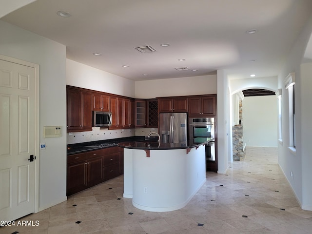 kitchen with an island with sink, sink, tasteful backsplash, appliances with stainless steel finishes, and a breakfast bar