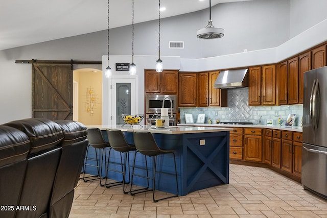 kitchen with pendant lighting, stainless steel appliances, a barn door, and wall chimney range hood