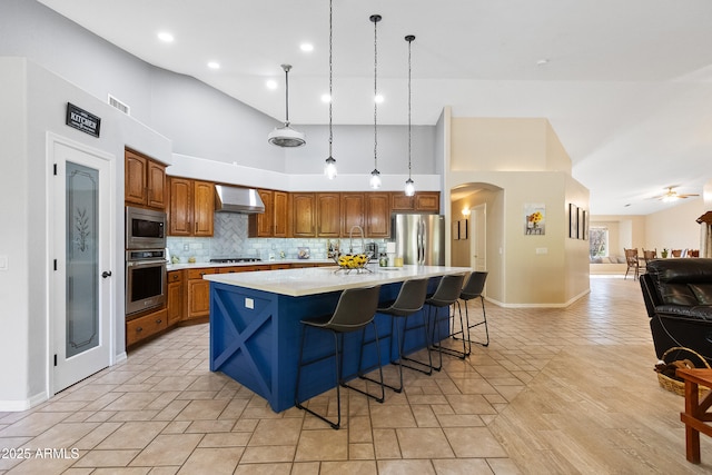 kitchen with a breakfast bar area, decorative light fixtures, a center island, appliances with stainless steel finishes, and wall chimney range hood