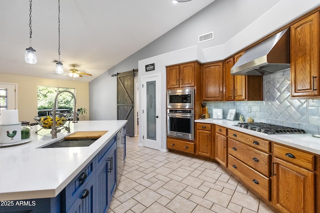 kitchen with wall chimney exhaust hood, sink, appliances with stainless steel finishes, pendant lighting, and a barn door