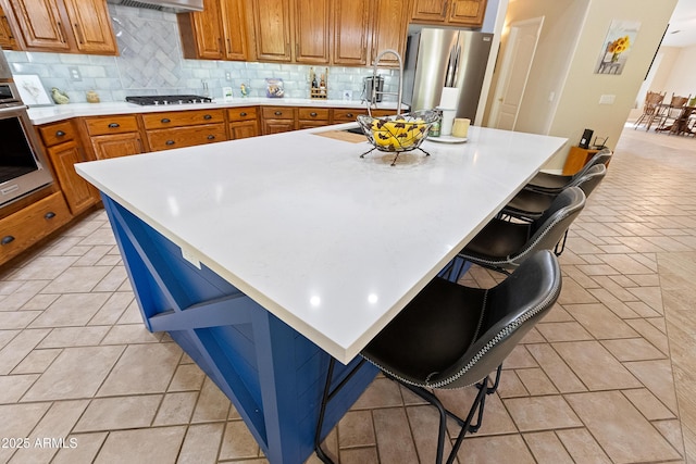 kitchen featuring range hood, tasteful backsplash, a kitchen breakfast bar, stainless steel appliances, and a spacious island