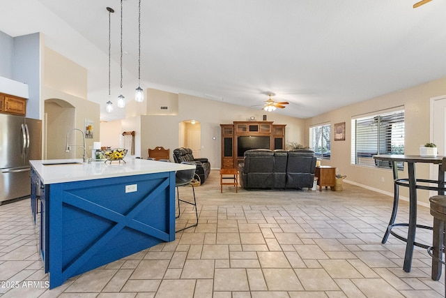 kitchen featuring sink, stainless steel fridge, a breakfast bar area, a kitchen island with sink, and hanging light fixtures