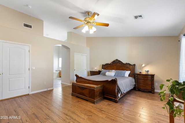 bedroom featuring light hardwood / wood-style flooring, ensuite bathroom, ceiling fan, and vaulted ceiling