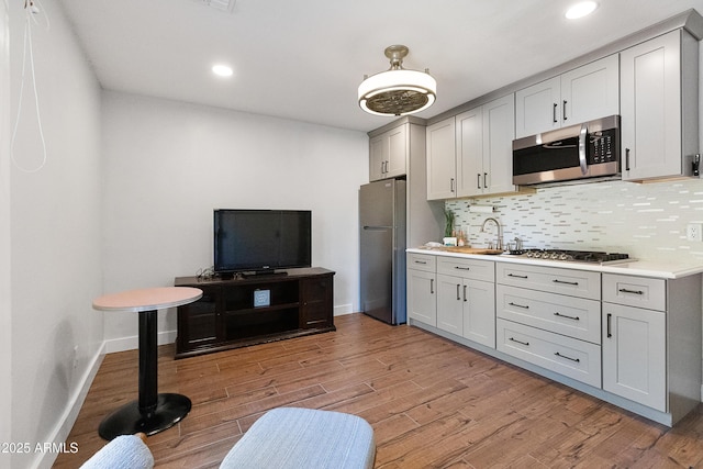 kitchen with gray cabinets, sink, backsplash, stainless steel appliances, and light hardwood / wood-style flooring