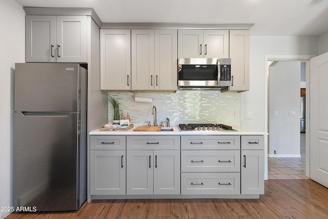 kitchen featuring sink, gray cabinets, appliances with stainless steel finishes, tasteful backsplash, and wood-type flooring