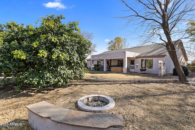 rear view of property featuring a fire pit, a patio area, and a hot tub