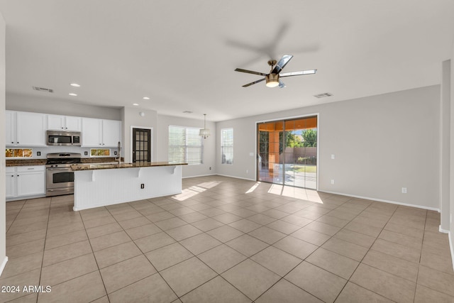 kitchen featuring white cabinetry, ceiling fan, stainless steel appliances, dark stone counters, and a breakfast bar area