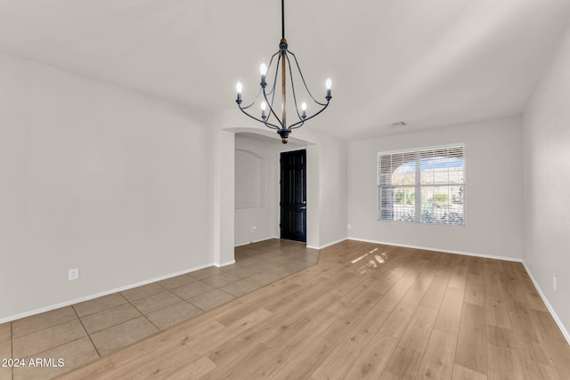 empty room featuring an inviting chandelier and light hardwood / wood-style flooring