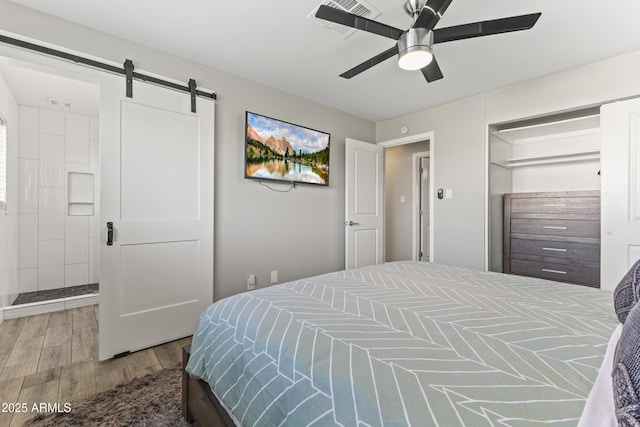 bedroom featuring ceiling fan, a barn door, and hardwood / wood-style floors