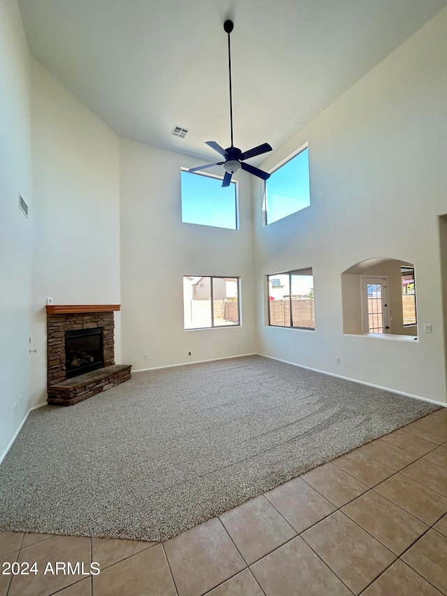 unfurnished living room featuring a high ceiling, ceiling fan, a fireplace, and light tile patterned flooring