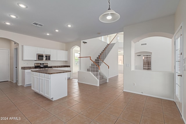 kitchen with light tile patterned flooring, hanging light fixtures, white cabinetry, appliances with stainless steel finishes, and a center island