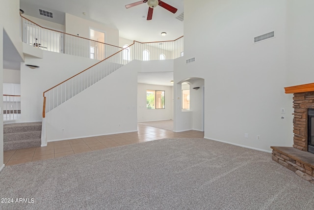 unfurnished living room with light carpet, a fireplace, a towering ceiling, and ceiling fan