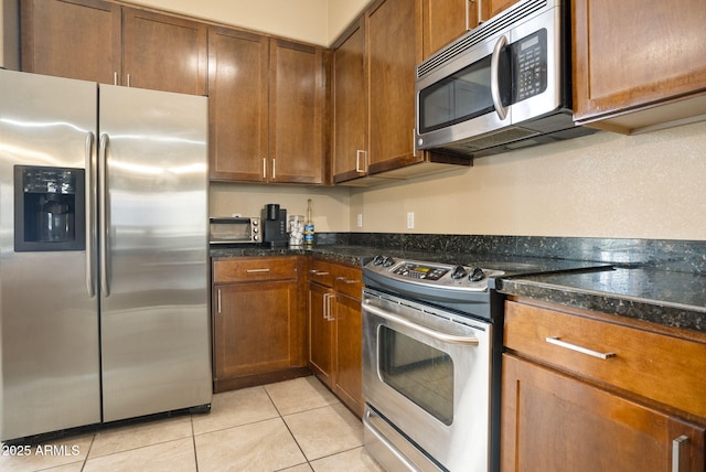 kitchen featuring dark stone countertops, light tile patterned floors, and stainless steel appliances