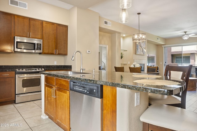 kitchen featuring pendant lighting, sink, light tile patterned floors, a kitchen island with sink, and stainless steel appliances