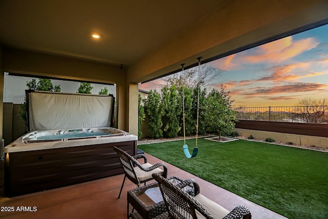 patio terrace at dusk featuring a hot tub and a yard