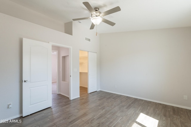 unfurnished bedroom with a closet, baseboards, visible vents, a walk in closet, and wood finished floors