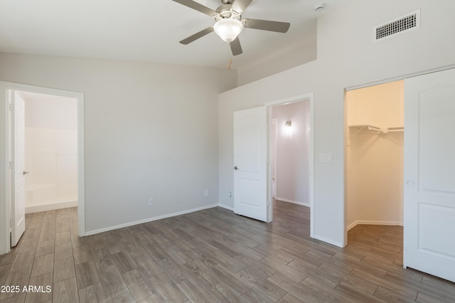 unfurnished bedroom featuring a closet, wood finished floors, visible vents, a walk in closet, and baseboards