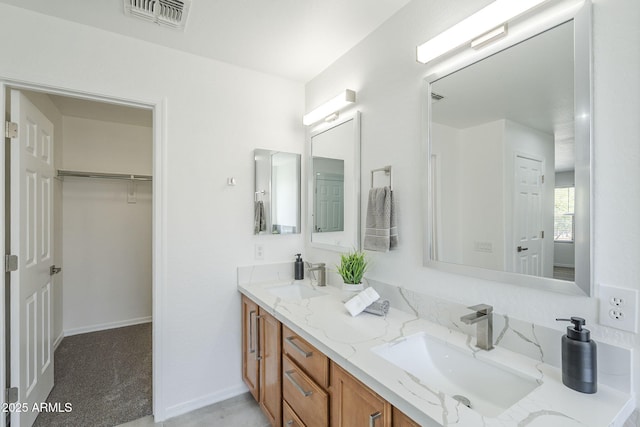 bathroom with a walk in closet, a sink, visible vents, and double vanity