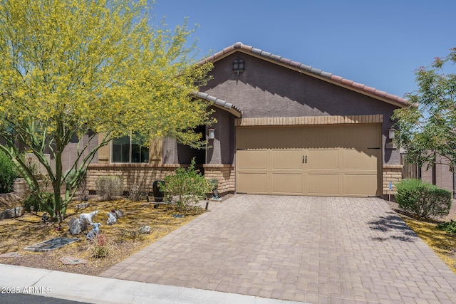view of front of property featuring a garage, stone siding, decorative driveway, stucco siding, and a tiled roof