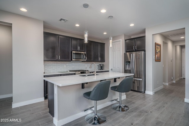 kitchen with decorative backsplash, a breakfast bar area, appliances with stainless steel finishes, baseboards, and light wood finished floors