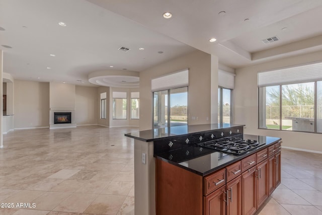 kitchen featuring a healthy amount of sunlight, stainless steel gas cooktop, a kitchen island, and dark stone counters