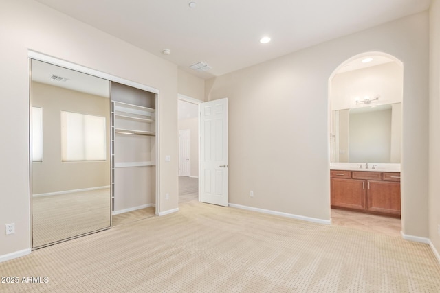 unfurnished bedroom featuring light carpet, sink, ensuite bath, and a closet