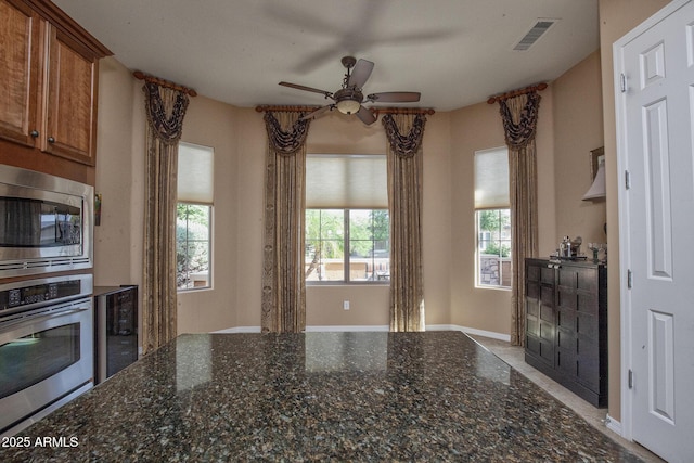 26293 W Runion Ln, Buckeye, AZ 85396 - kitchen with ceiling fan, brown cabinetry, dark stone counters, stainless steel appliances, and visible vents