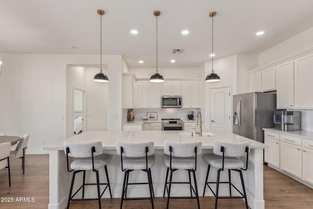 kitchen featuring stainless steel appliances, a sink, backsplash, wood finished floors, and white cabinetry