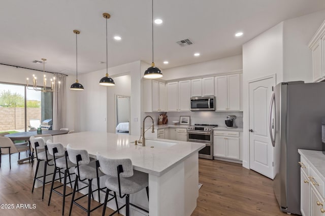 kitchen with appliances with stainless steel finishes, a sink, white cabinets, a center island with sink, and recessed lighting