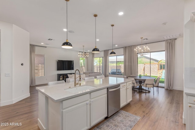 kitchen with a sink, a chandelier, open floor plan, stainless steel dishwasher, and light wood-style floors