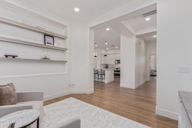 living area featuring light wood-style floors, baseboards, built in shelves, and recessed lighting