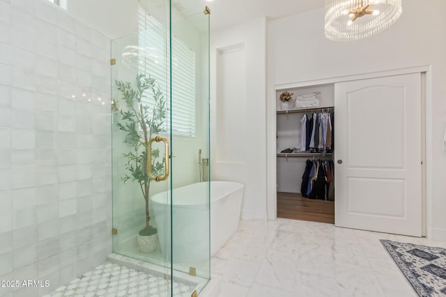 full bath featuring a freestanding tub, a shower with door, a chandelier, a walk in closet, and marble finish floors