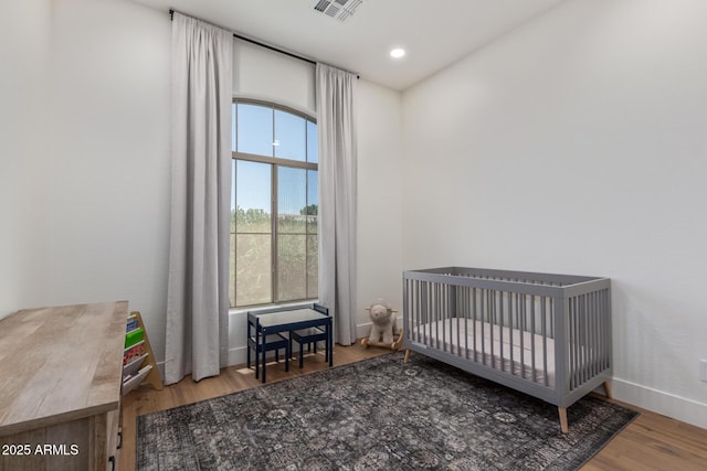 bedroom with wood finished floors, baseboards, and a nursery area