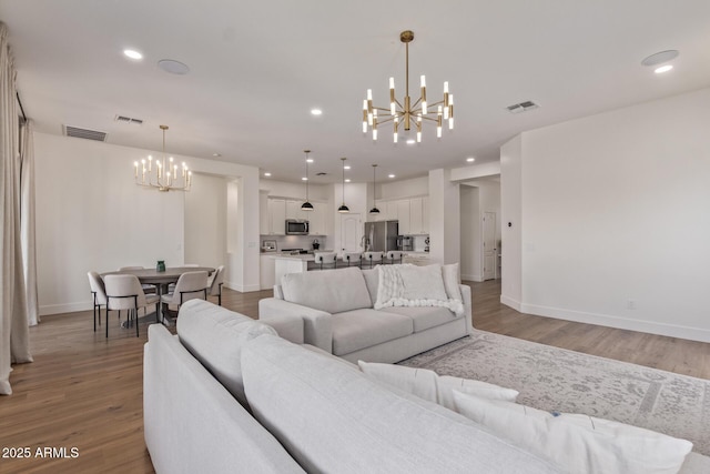 living area with a chandelier, light wood finished floors, baseboards, and recessed lighting