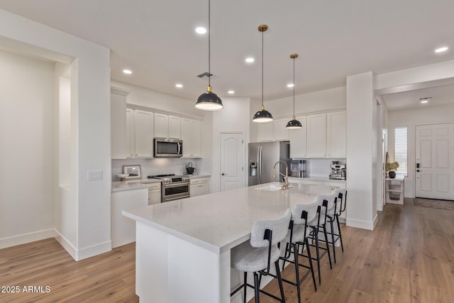 kitchen with appliances with stainless steel finishes, light wood-style floors, a kitchen breakfast bar, baseboards, and recessed lighting