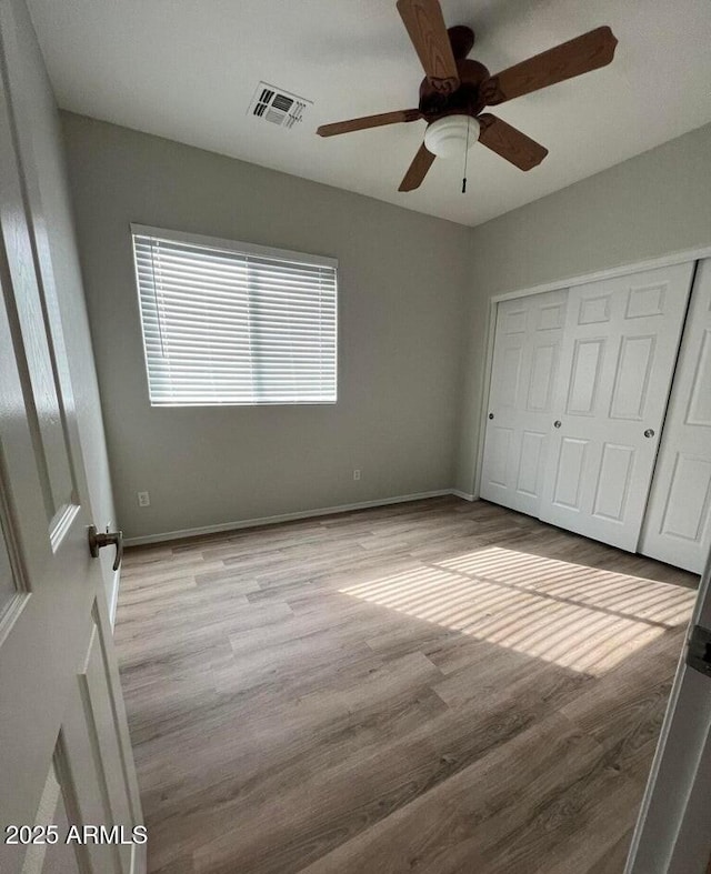 unfurnished bedroom featuring a closet, visible vents, ceiling fan, wood finished floors, and baseboards