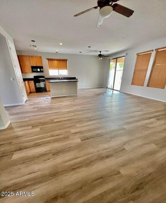 unfurnished living room with ceiling fan, light wood-style flooring, and baseboards