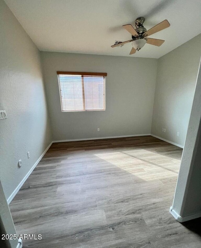 spare room with wood finished floors, a ceiling fan, and baseboards