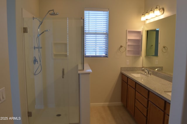 bathroom featuring wood finished floors, a sink, baseboards, double vanity, and a stall shower