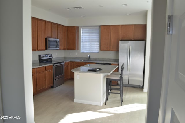 kitchen featuring light countertops, appliances with stainless steel finishes, a sink, a kitchen island, and a kitchen bar