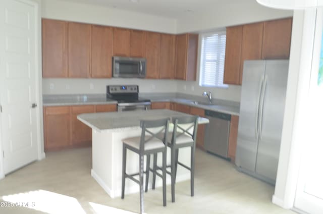 kitchen featuring a breakfast bar, a sink, appliances with stainless steel finishes, a center island, and brown cabinetry