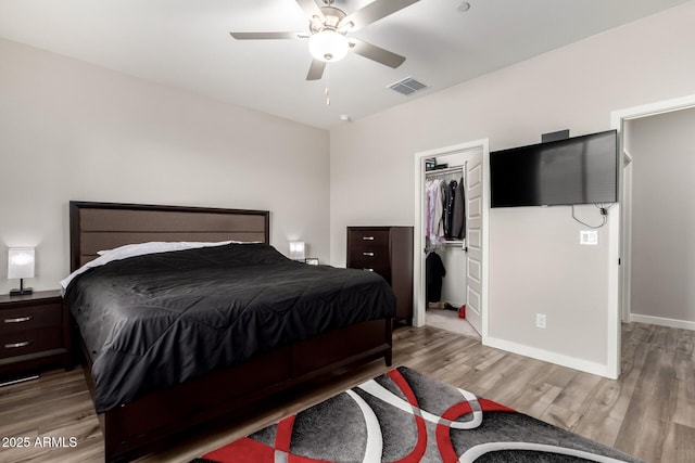 bedroom with wood finished floors, visible vents, baseboards, a spacious closet, and a closet